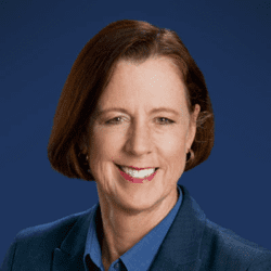 Headshot of Sara Boyd, woman with brown hair above her chin wearing a blue collared shirt and blazer in front of a blue background