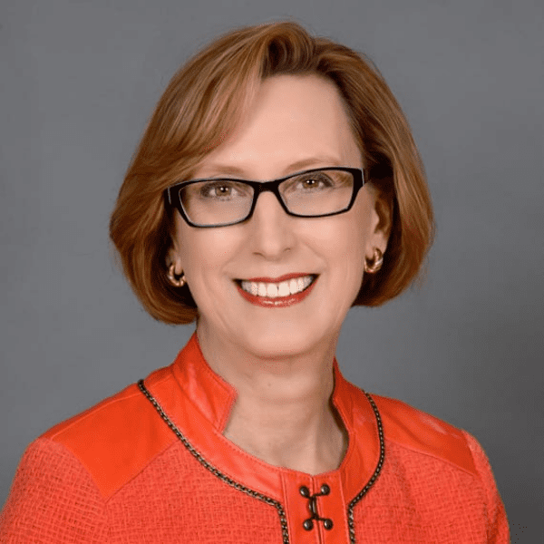 Roslyn Dawson Thompson headshot - white woman with black-framed glasses, short red hair, earrings, wearing a red blazer with black detailing